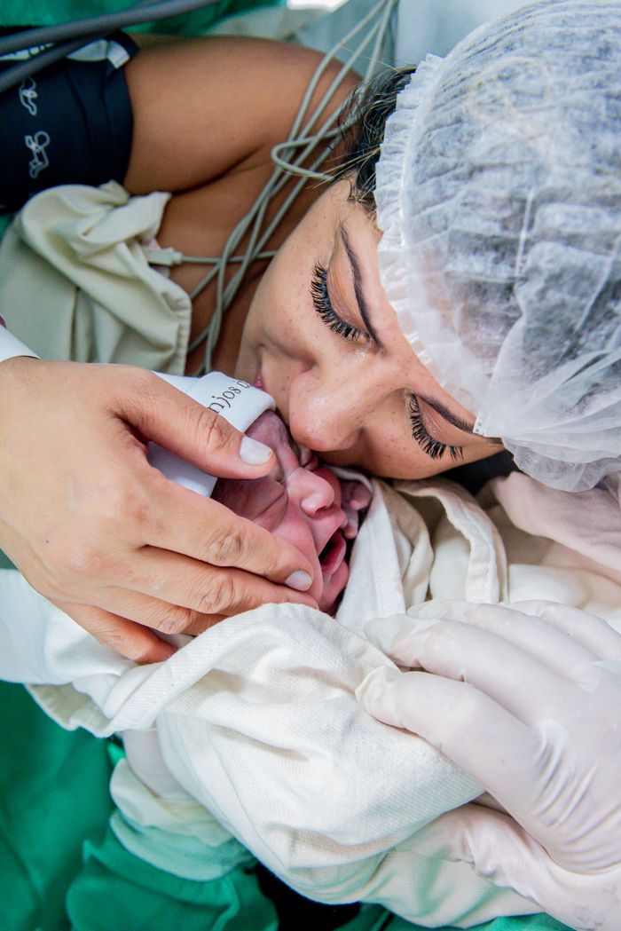 A mother lovingly embraces her newborn baby in a hospital setting, capturing a touching moment.